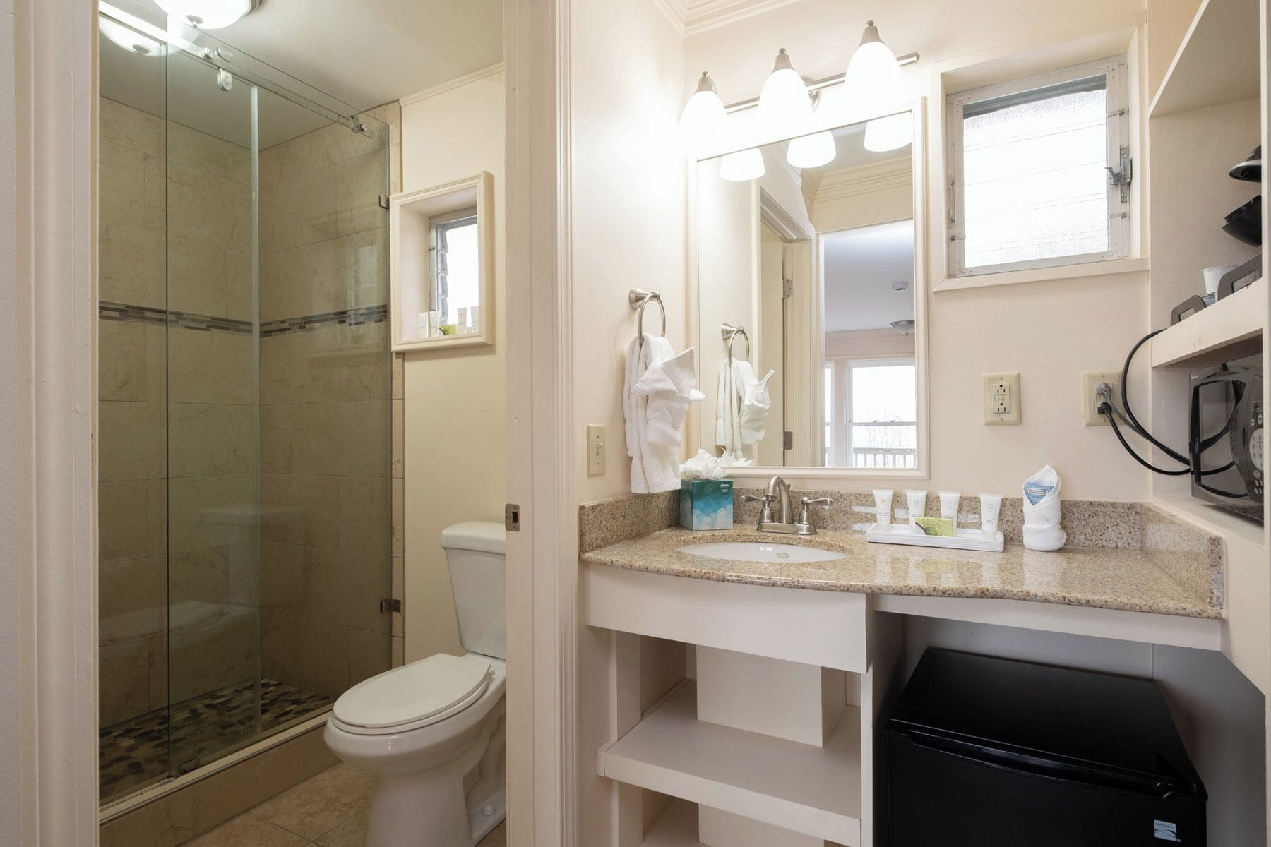 A bathroom with a glass shower enclosure, a toilet, a sink with a vanity, and a mirror with lights.