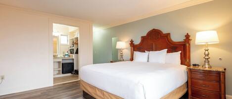 A hotel room with a large bed, wooden headboard, two bedside tables with lamps, a wardrobe, and a bathroom visible through an open door.