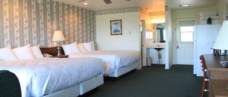 A hotel room with two beds, a desk, a chair, a ceiling fan, and a bathroom visible through an open door.
