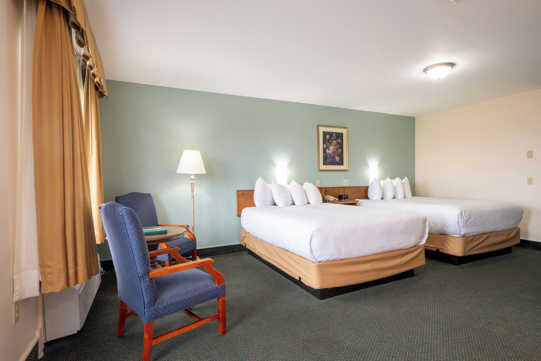 Une chambre d’hôtel avec deux lits, une chaise, un bureau, une lampe et un tableau au mur.