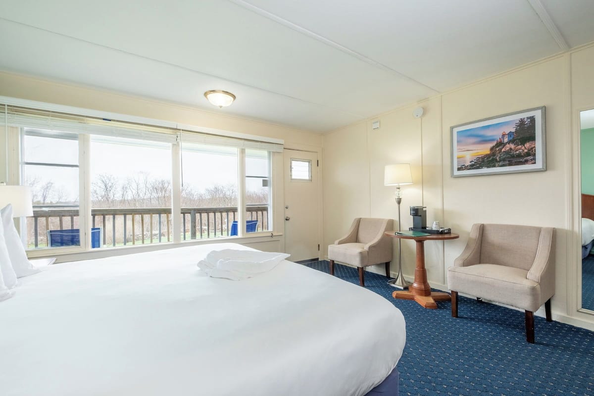 Una habitación de hotel con una cama grande, dos sillones, una mesita, una lámpara y un cuadro en la pared.