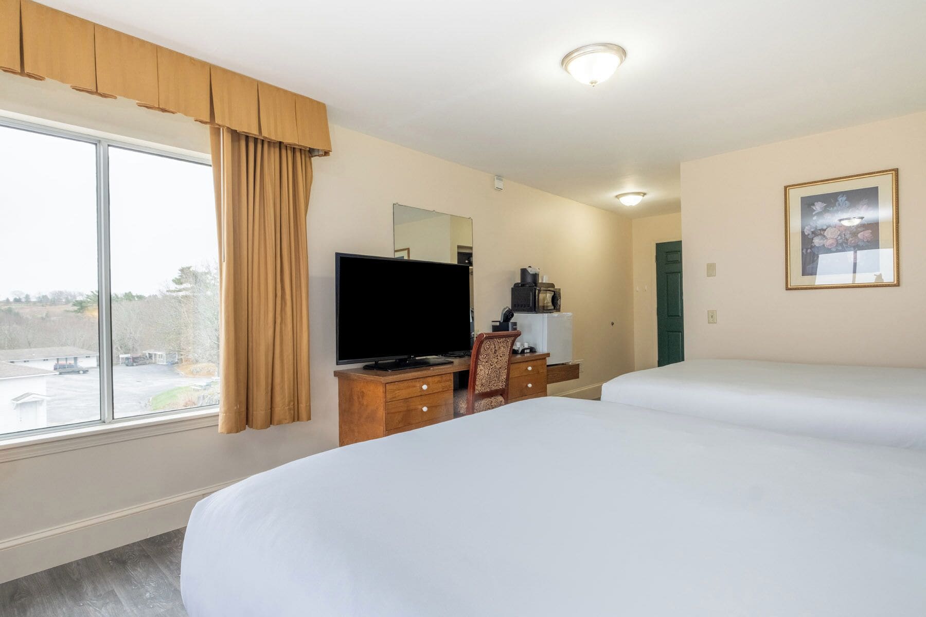 Une chambre d’hôtel dotée d’une grande fenêtre, d’un téléviseur à écran plat, d’un bureau avec un ordinateur, d’un lit et d’un tableau encadré au mur.
