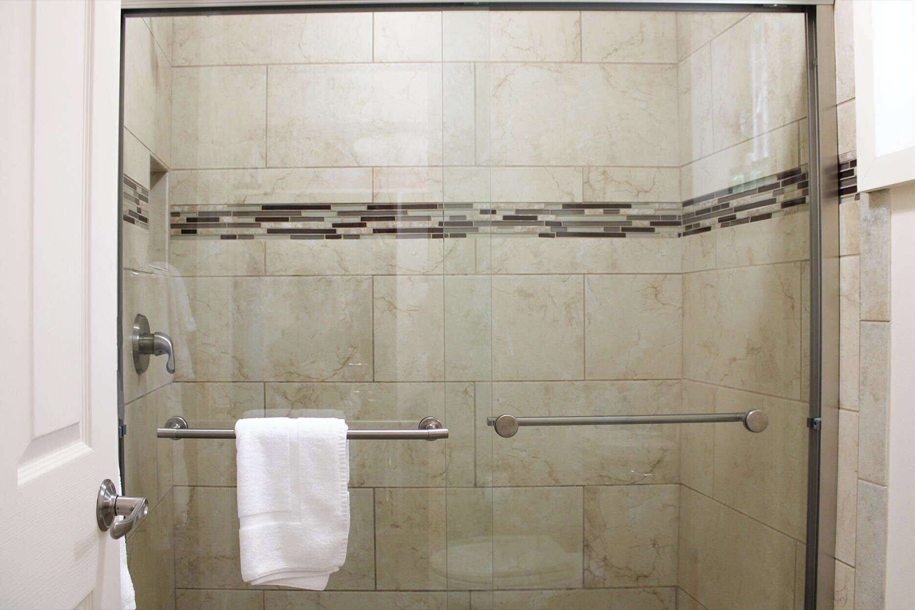 A glass-enclosed shower with a white towel hanging on a metal towel bar.