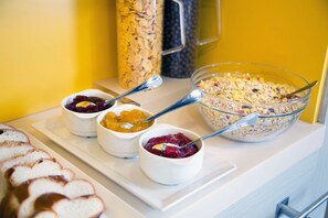 Ein Frühstücksbuffet mit verschiedenen Speisen, darunter Brot, Müsli und Fruchtkompotte.