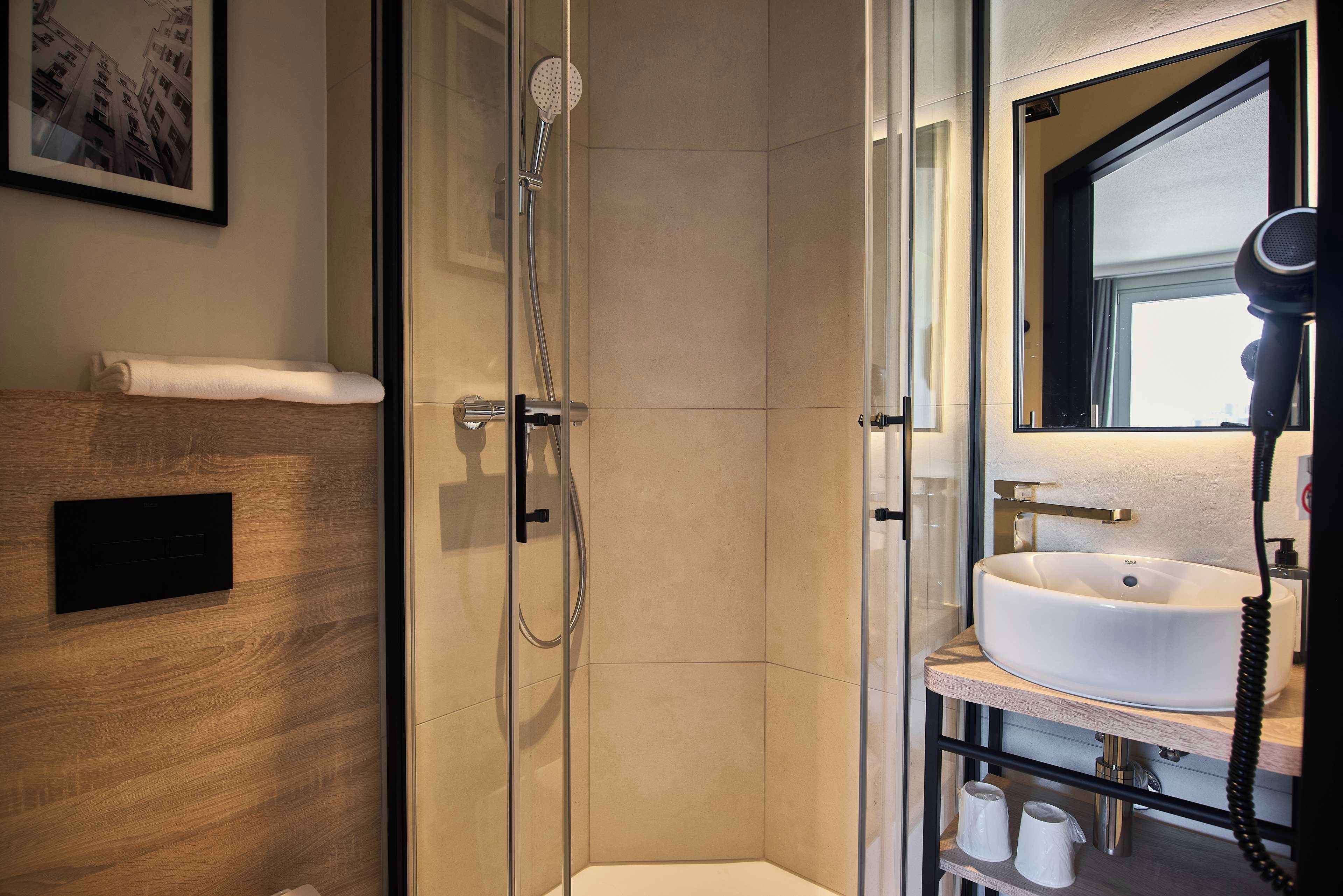 A modern bathroom with a glass-enclosed shower, a white sink, and a hairdryer.