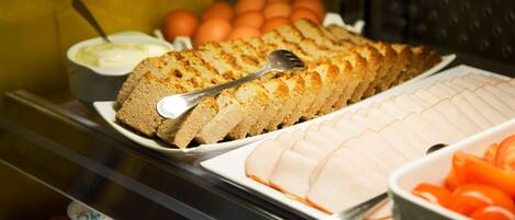 A buffet with various food items including a loaf of bread, a bowl of dip, and sliced tomatoes.