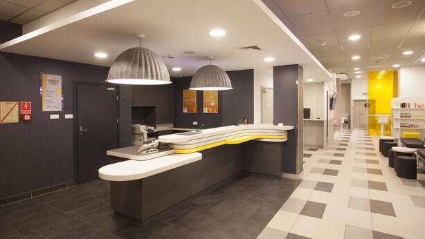 A modern reception area with a curved counter, two pendant lights, and a check-in desk. - Premiere Classe Warszawa Centrum (Warsaw)