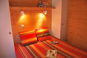 A small, cozy room with a wooden headboard, two pillows, a tray with a cup and cookies, and a shelf with books.