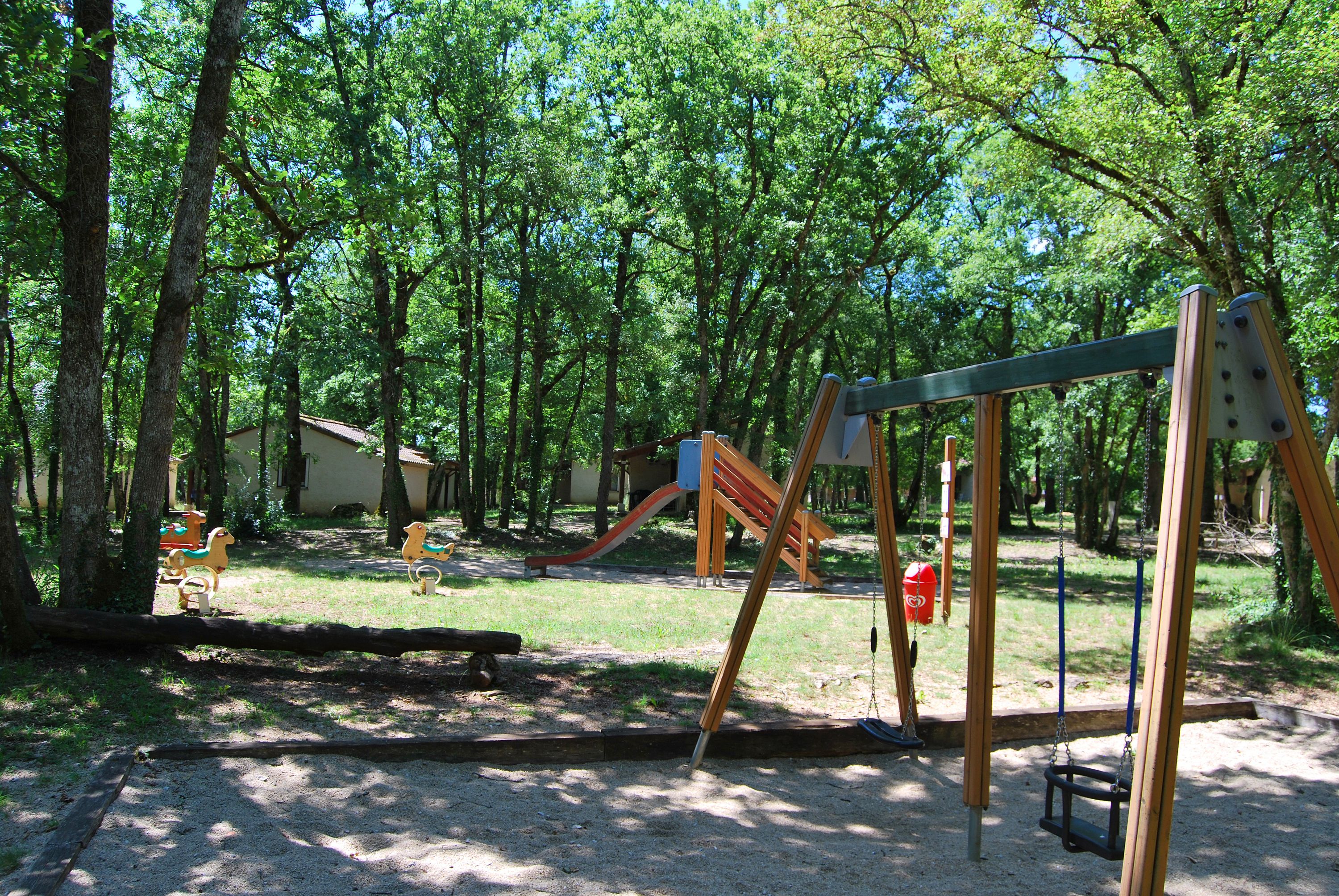 A playground with swings and slides, surrounded by trees.