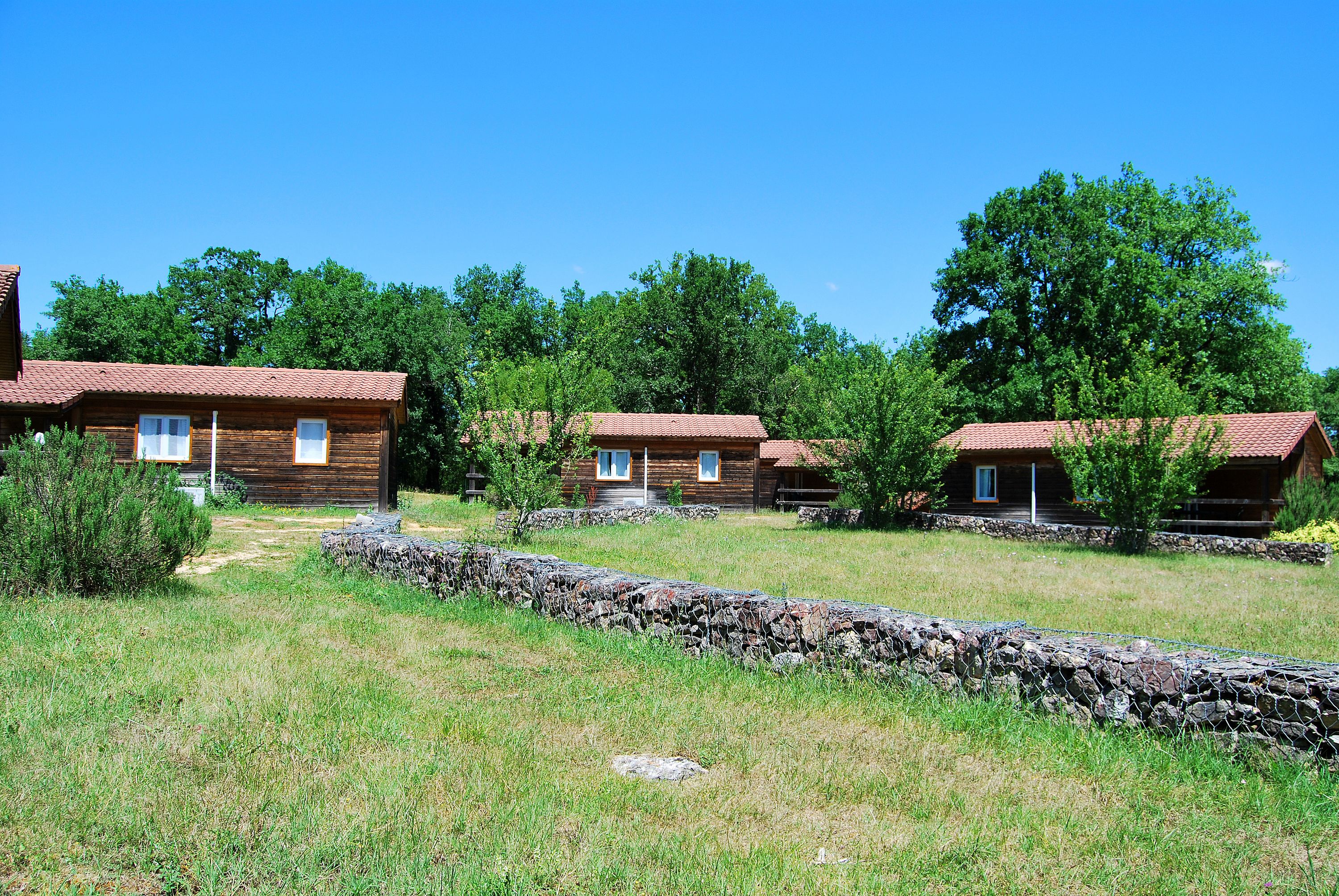 A row of log cabins with stone walls and a clear blue sky.