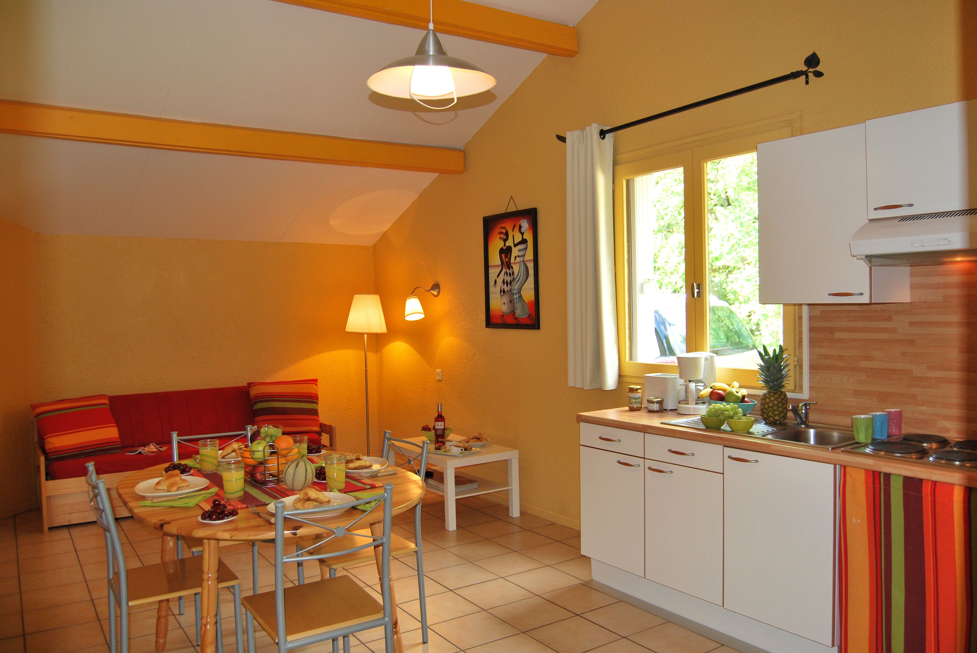 A cozy kitchen with a dining area, featuring a wooden table, chairs, and a red sofa.