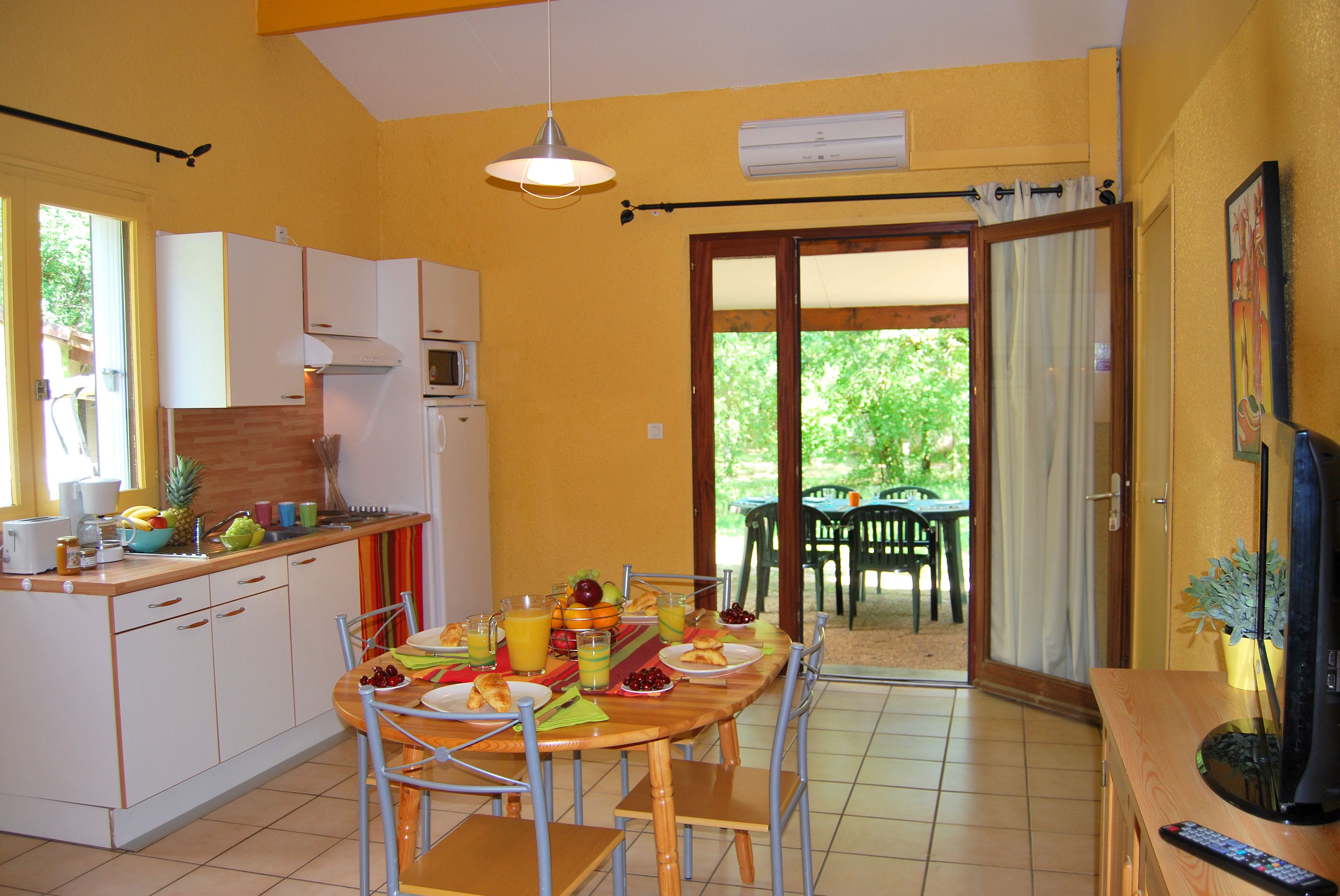 Cocina compacta con gabinetes blancos, microondas y comedor con mesa y sillas de madera.