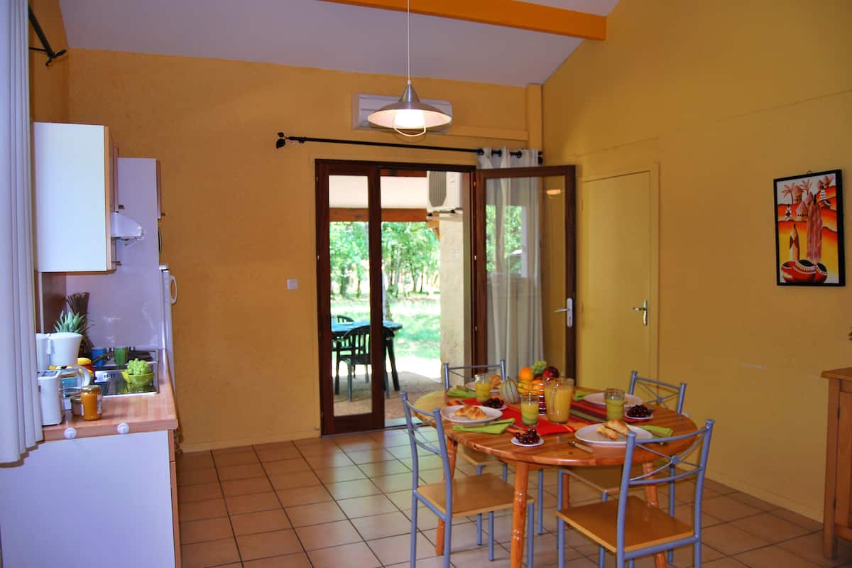 A dining area with a table set for four, a kitchen area with a refrigerator and a sink, and a sliding glass door leading to an outdoor patio.