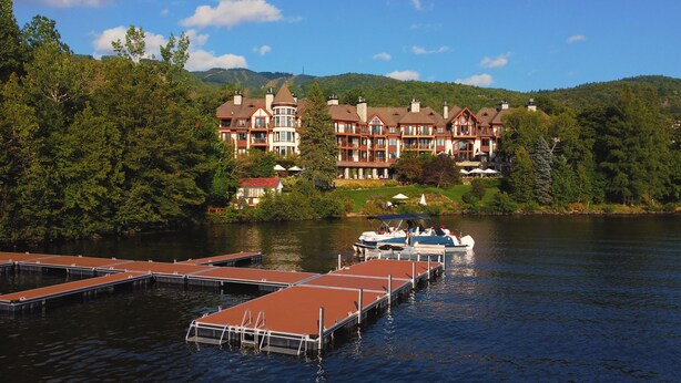 A lakeside hotel with multiple buildings, docked boats, and lush greenery.