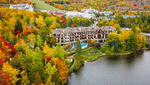 A large, multi-story hotel with a pool and a lake view, surrounded by autumn-colored trees.