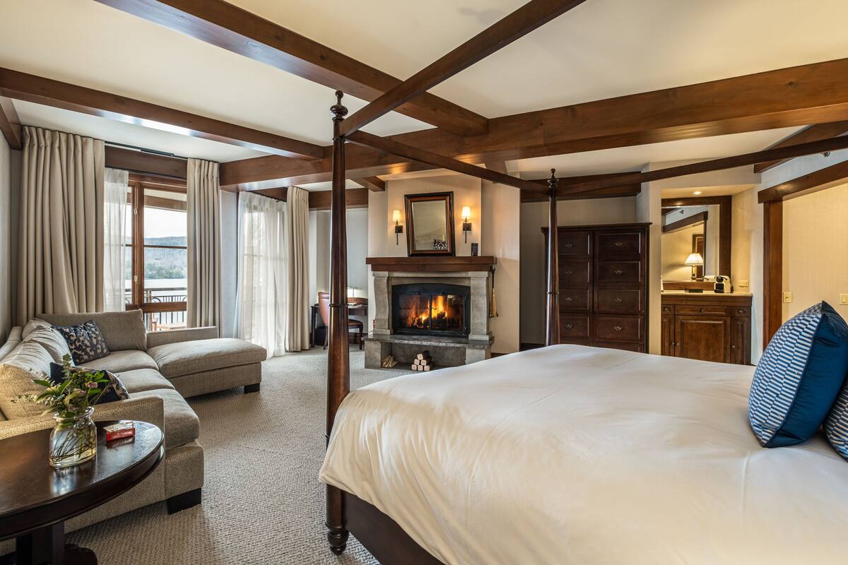 Een hotelkamer met een groot bed, een bank, een open haard en uitzicht op de omgeving.