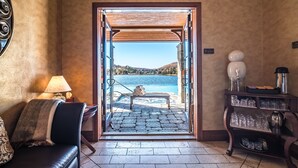 A hotel lobby with a view of a lake and mountains, a wooden bench, a lamp, and a shelf with glassware.