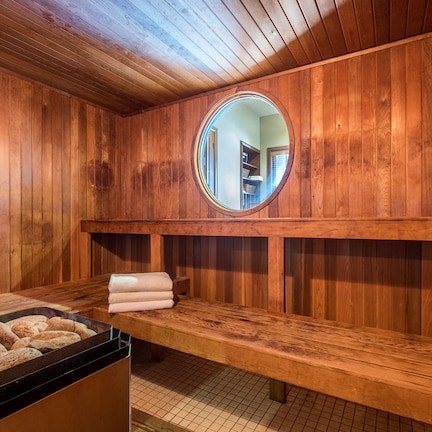 A sauna room with wooden walls, a round mirror, a bench, and a tray with towels.