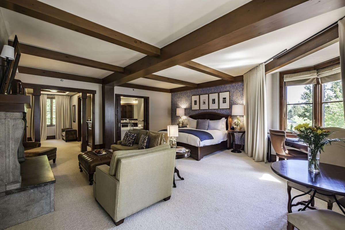 Een ruime kamer met een groot bed, een zithoek met een bank en fauteuils, een eettafel, en uitzicht op het natuurlijke landschap door een raam.
