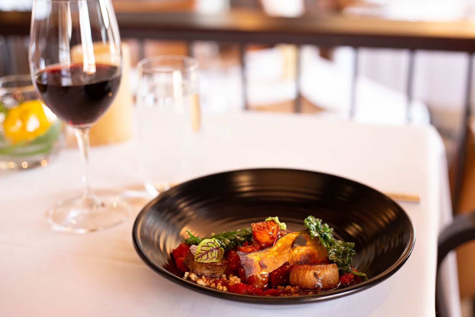 A dining table with a black plate of food, a glass of red wine, and a glass of water.