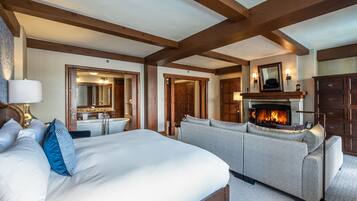 A hotel room with a large bed, a sofa, a fireplace, and wooden beams on the ceiling.