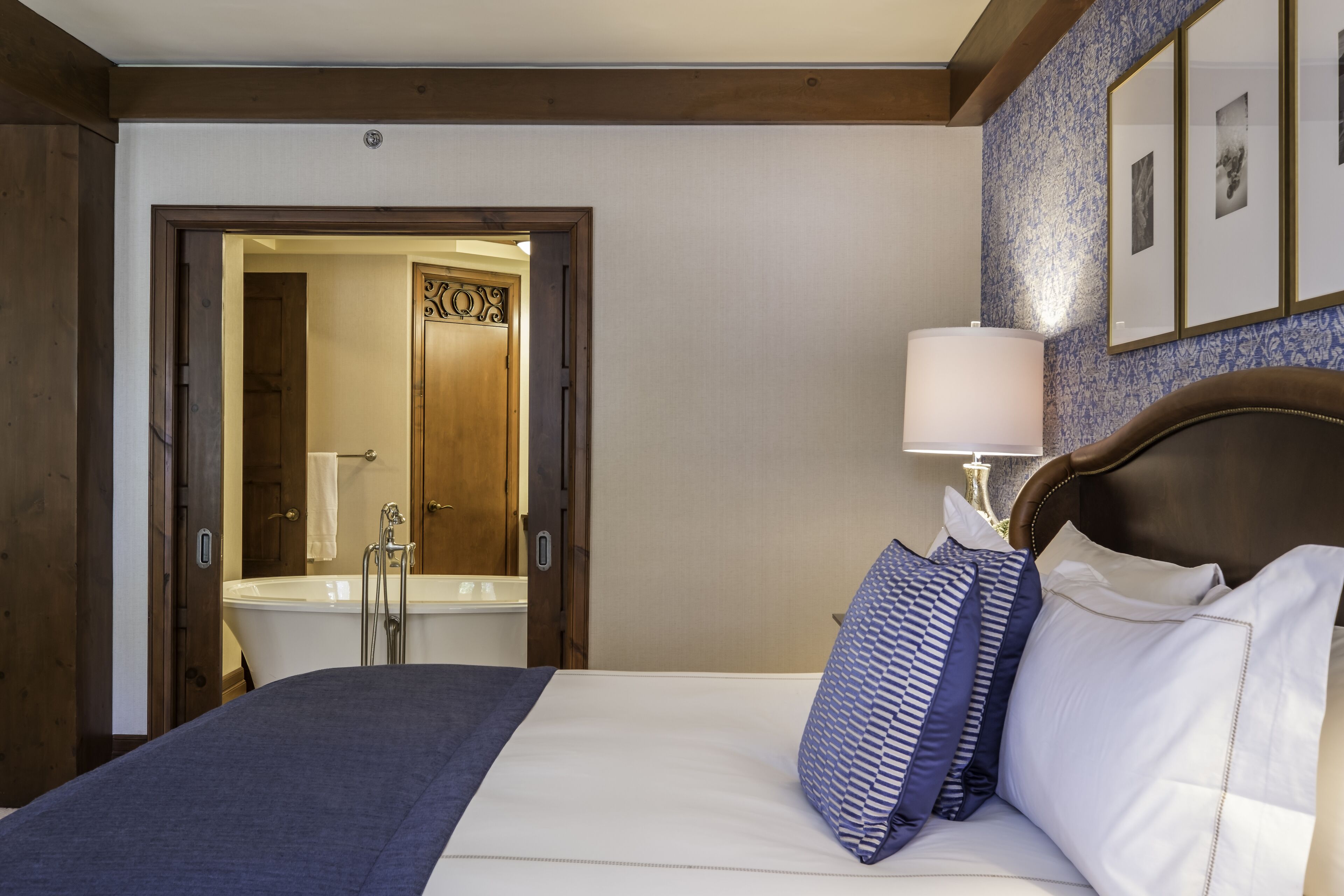 Une chambre d’hôtel avec un grand lit, une tête de lit en bois, une lampe de chevet et une salle de bain visible à travers une porte ouverte.