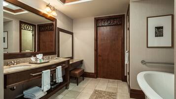 Un baño con tocador doble, un espejo grande, una puerta de madera, una bañera y un pequeño banco.