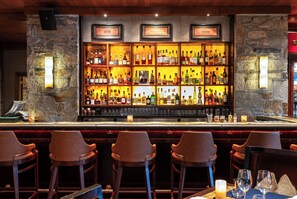 A bar with a stone wall and wooden bar counter, featuring multiple shelves of bottles and glasses.