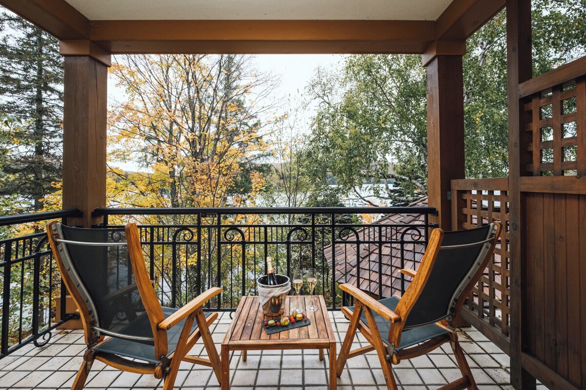 A wooden deck with two chairs and a table, a bottle of champagne, and a glass of wine.