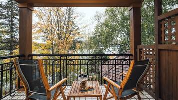 A wooden deck with two chairs and a table, a bottle of champagne, and a glass of wine.