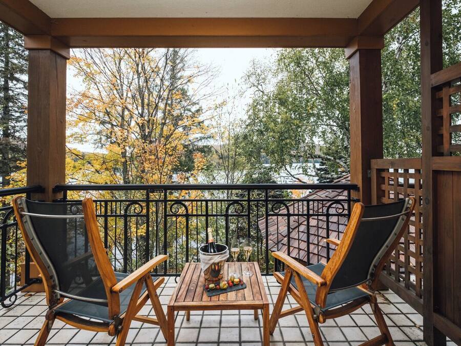 A wooden deck with two chairs and a table, a bottle of champagne, and a glass of wine.