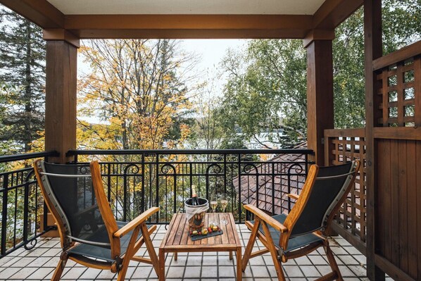 Terraza de madera con dos sillas, una mesa, una botella de champán y una copa de vino.
