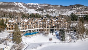 A large resort with multiple buildings, a swimming pool, and a snowy mountain backdrop.