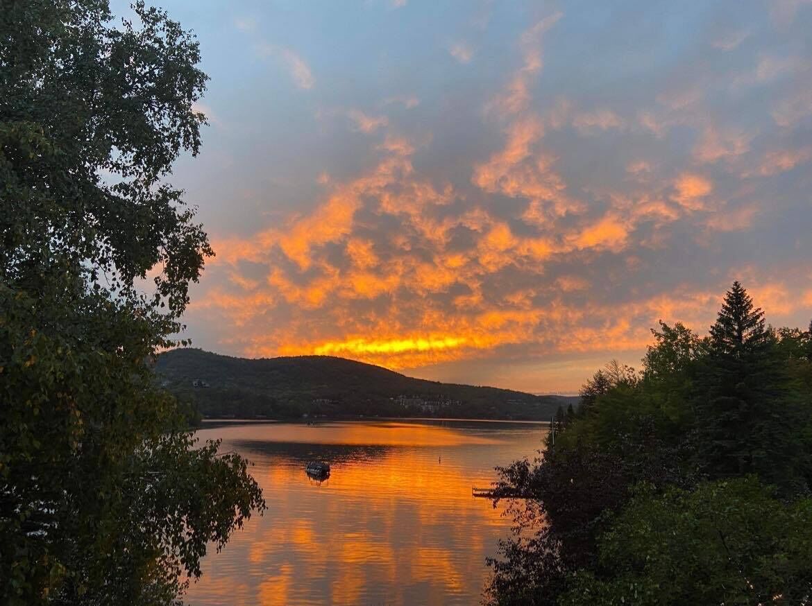 A lake with a sunset, surrounded by trees and hills.