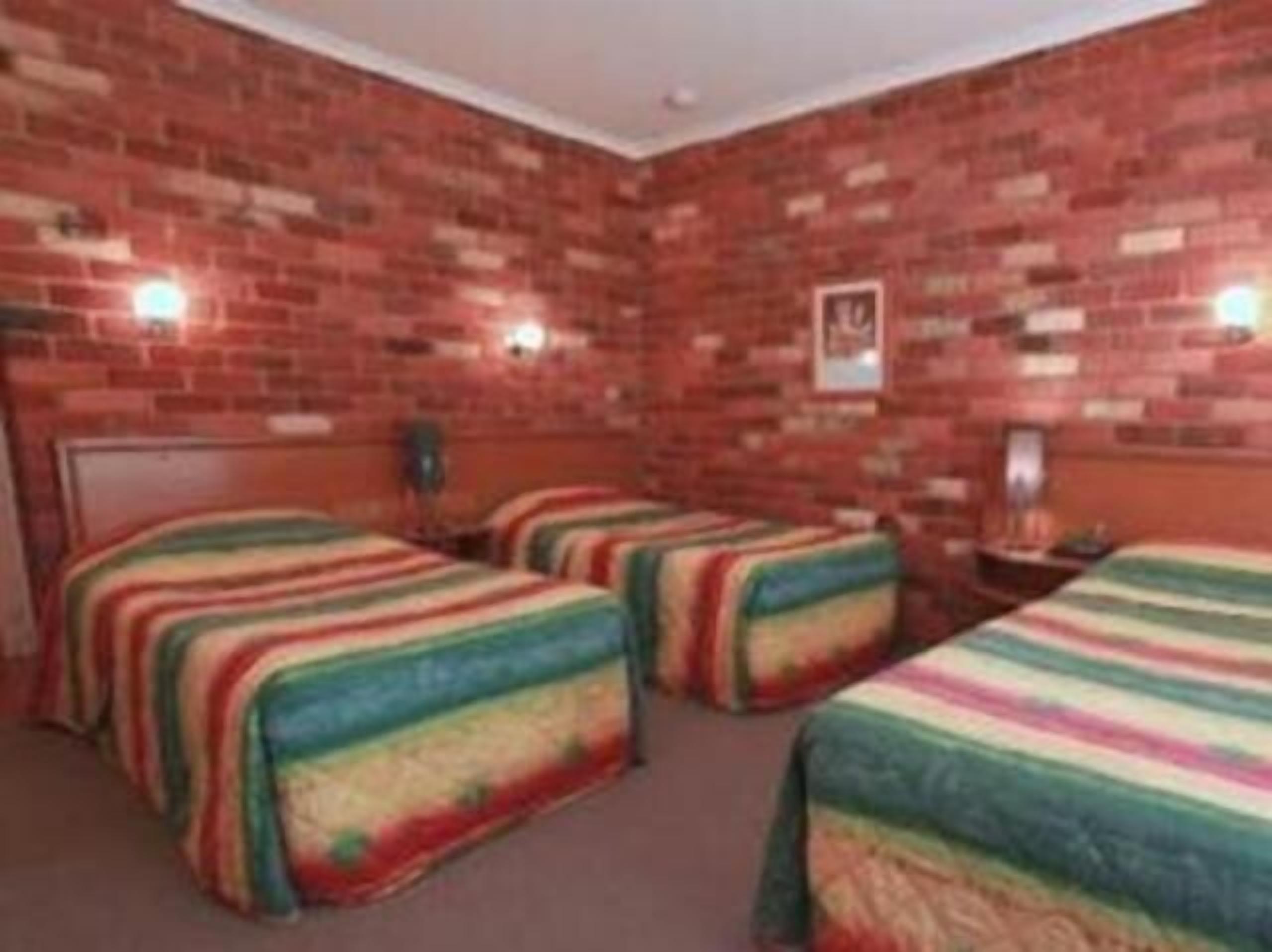 A room with brick walls, two beds with colorful striped bedding, a small table, and a framed picture on the wall.