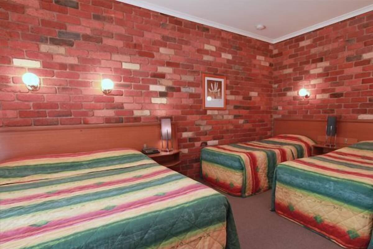 A room with four beds, brick walls, and wall-mounted lights.