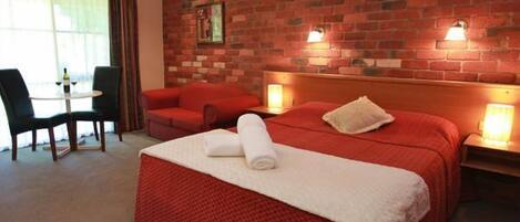 Ein Hotelzimmer mit Backsteinwand, einem roten Bett, einer roten Couch, einem kleinen Tisch mit einer Flasche und zwei Nachttischlampen.