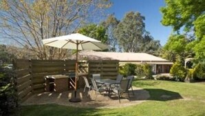 Una terraza de madera con mobiliario exterior, incluyendo una mesa y sillas, y una sombrilla grande que proporciona sombra.