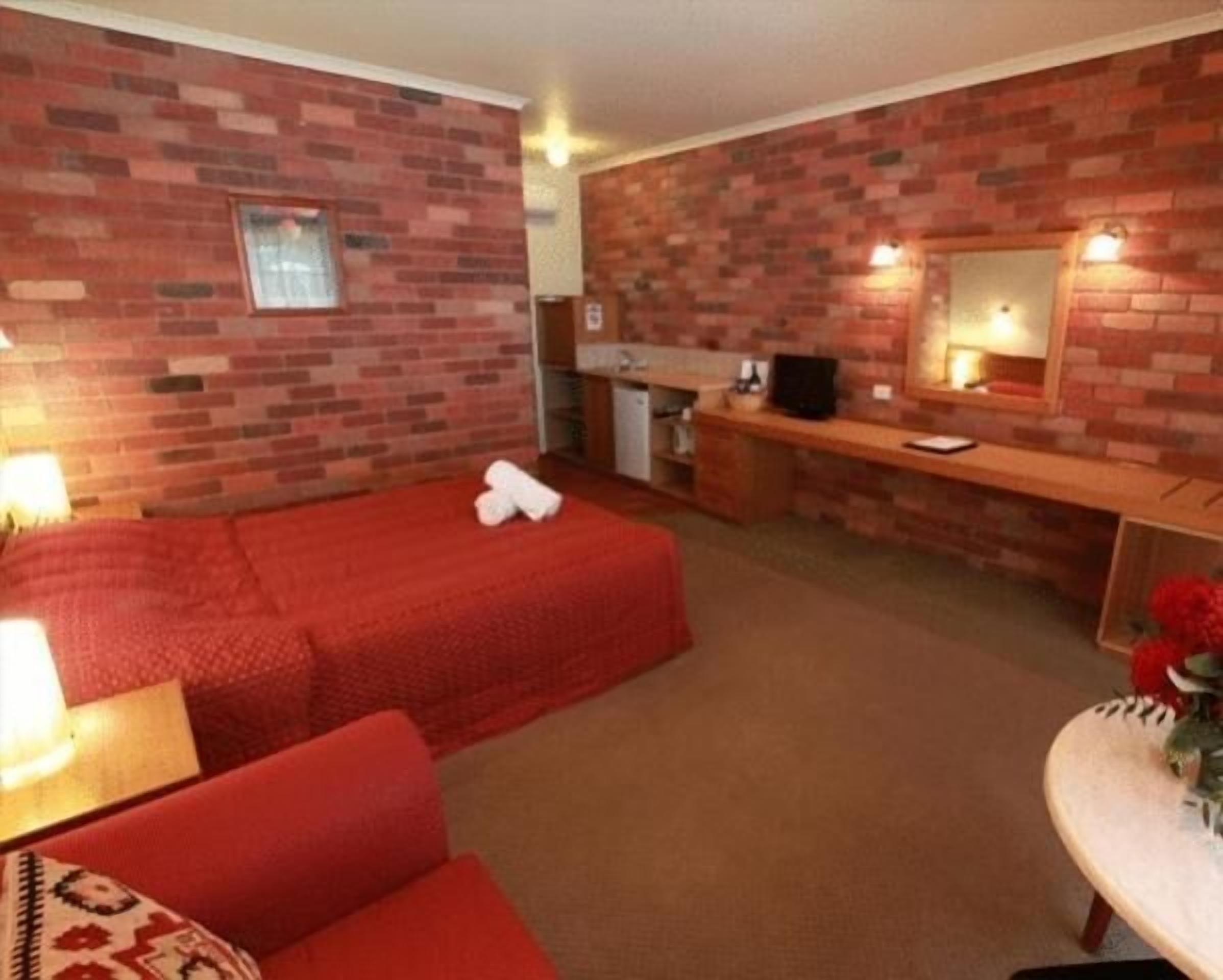 A room with a brick wall, a bed, a desk, and a mirror.