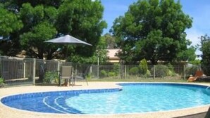 Una piscina con borde de azulejos, rodeada por una valla y árboles.
