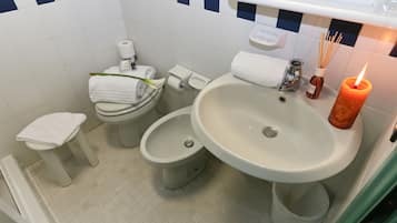 A bathroom with a toilet, bidet, sink, and a candle.