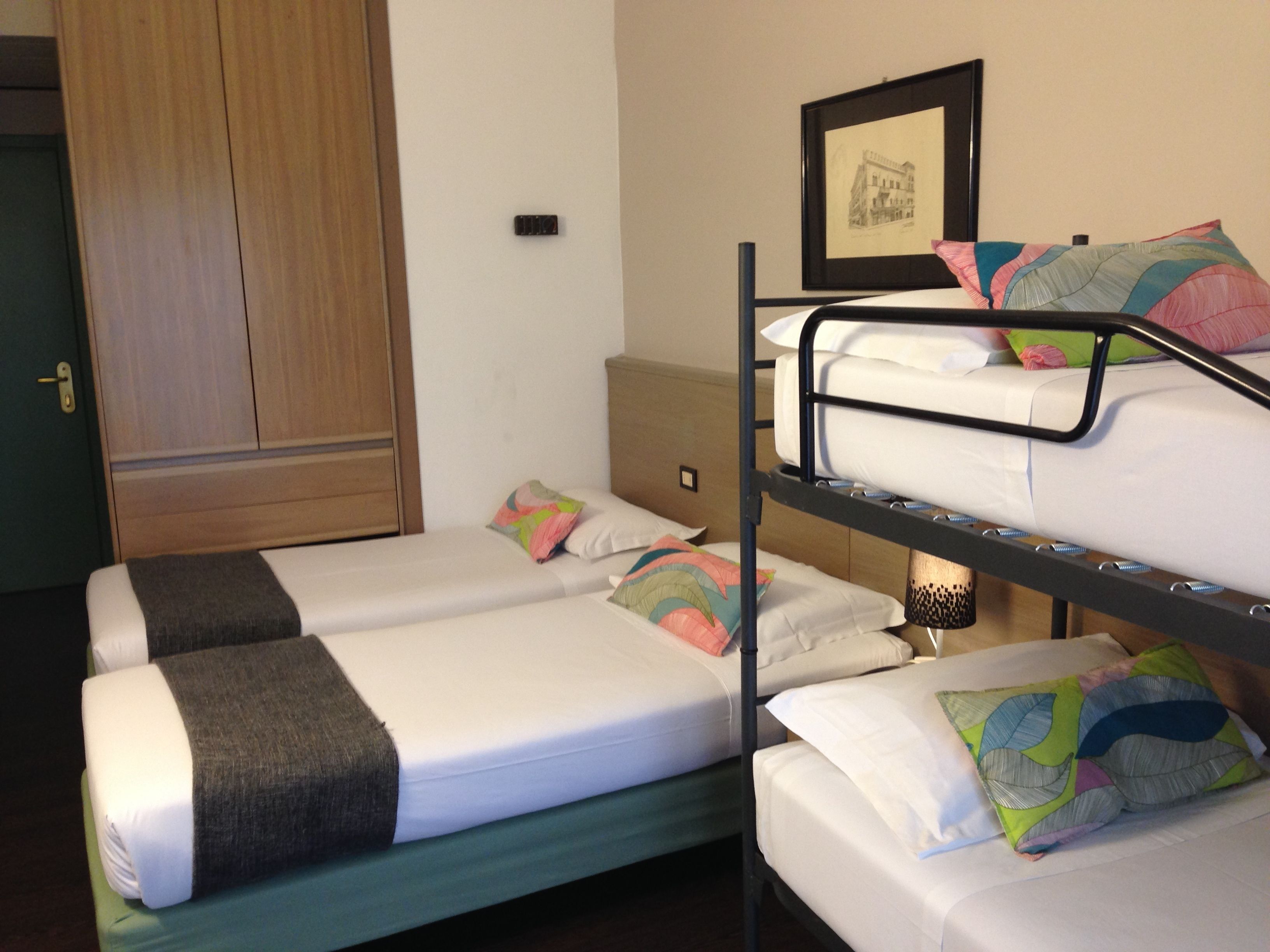A dormitory-style room with bunk beds, a wardrobe, and a framed picture on the wall.