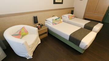 A hotel room with two single beds, a chair, a nightstand, and a wardrobe.