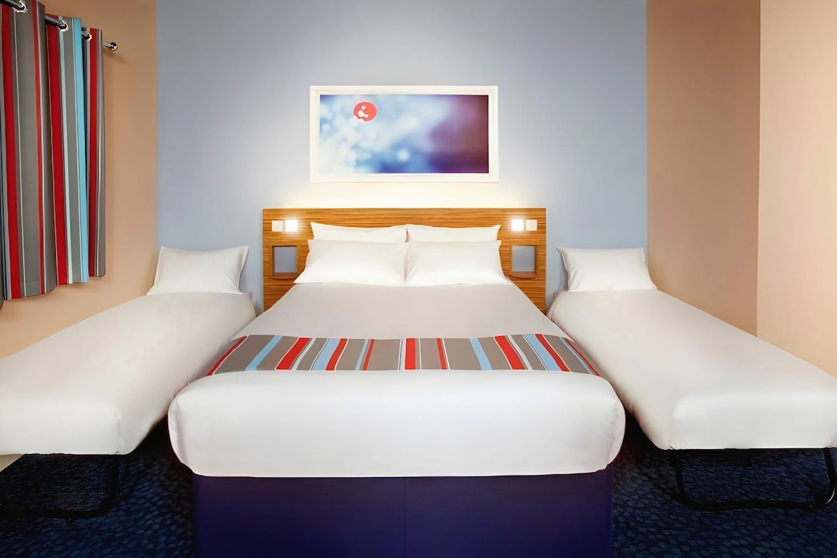 Una habitació d'hotel amb un llit, dues taules de nit, un quadre penjat a la paret i un edredó rayat.