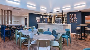A modern bar cafe with round tables and chairs, a counter with a coffee machine, and a blue and white color scheme. - Travelodge London Central Southwark (London)