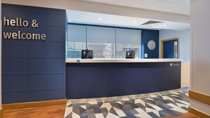 A reception area with a 'hello & welcome' sign, a reception desk, a clock, and a patterned floor. - Travelodge London Central Southwark (London)