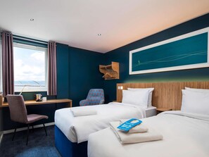 Une chambre d’hôtel avec deux lits, un bureau, une chaise, une fenêtre avec des rideaux et une œuvre d’art accrochée au mur.