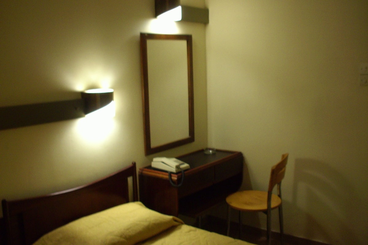 A hotel room with a bed, a desk with a chair, a telephone, and a wall-mounted mirror.