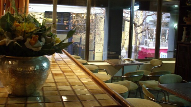 A restaurant interior with a tiled floor, a large vase with flowers, and a view of the street outside. - Claridge Hotel (Athens)