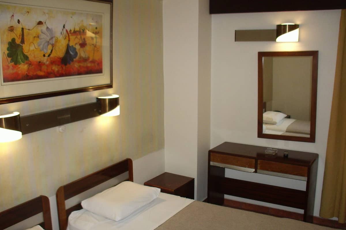 A hotel room with two beds, a bedside table, a dresser, a mirror, and a painting on the wall.